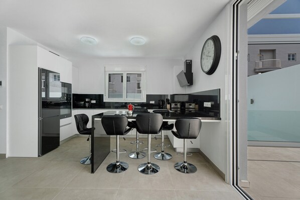 Una cocina moderna con una isla central, taburetes de bar y un gran reloj de pared.