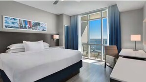 A hotel room with a large bed, a desk, a chair, and a balcony with a view. - Charming 2-bedroom beachfront resort near water parks and golf (Myrtle Beach)