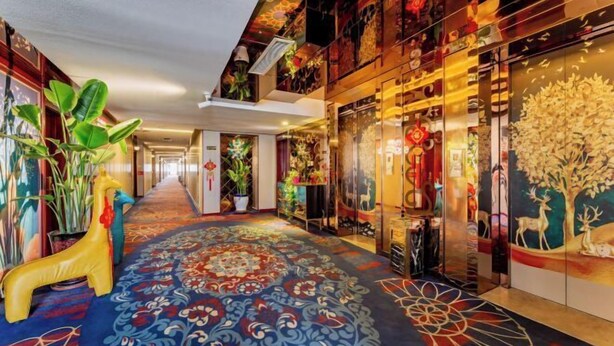 Un pasillo de hotel con alfombra estampada, plantas decorativas y obras de arte en las paredes.