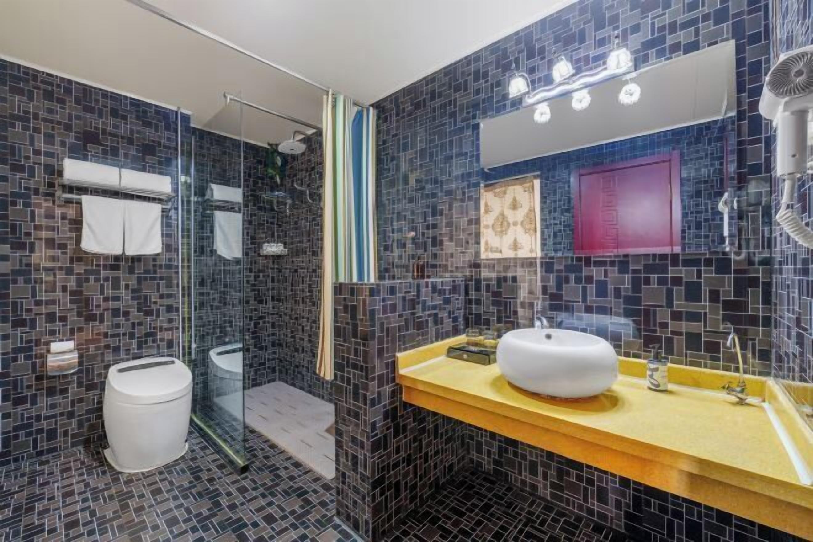 Un bagno moderno con box doccia in vetro, un water bianco, un lavabo con piano di appoggio giallo e uno specchio con luci.