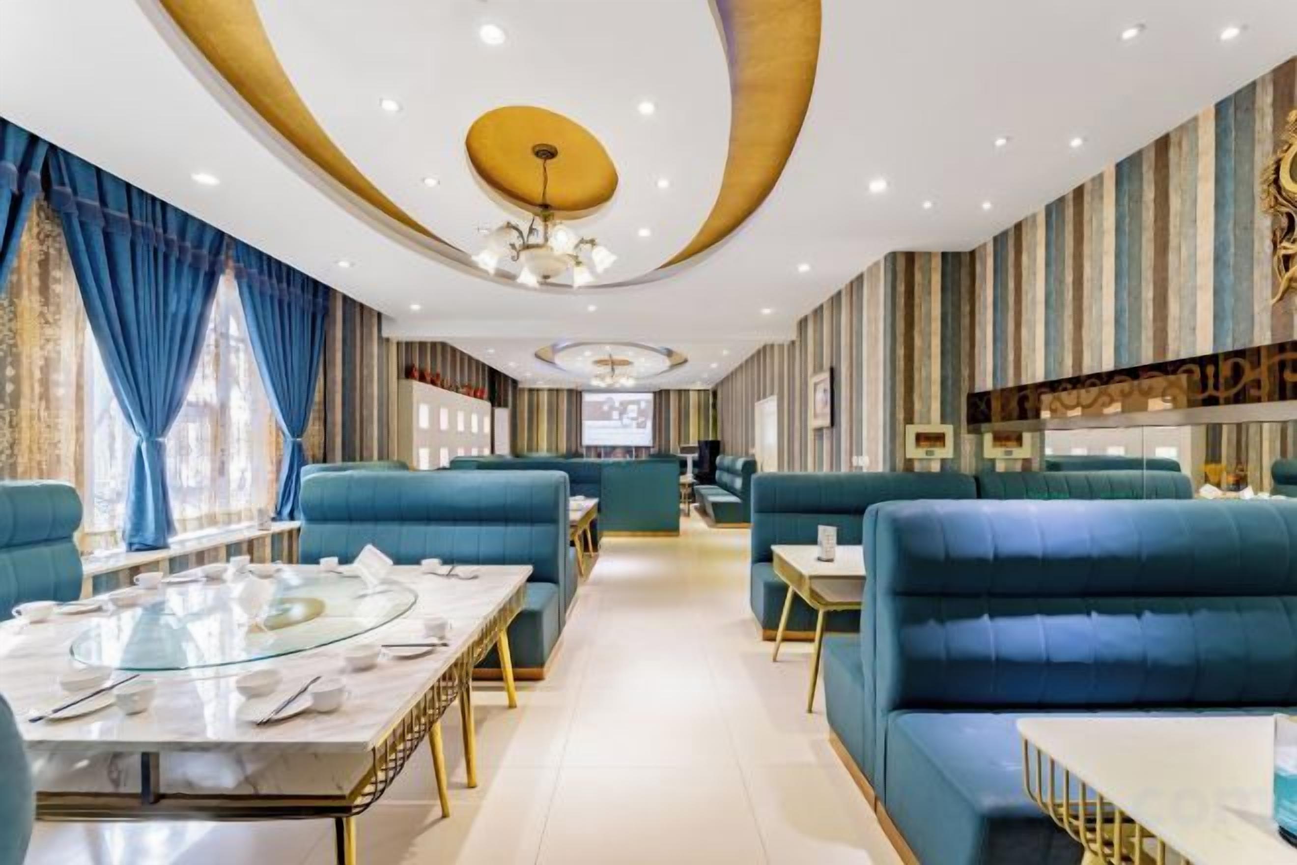 A modern dining area with blue upholstered seating, a glass table, and a chandelier.