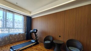 Una habitación con una cinta de correr, sillas de mimbre, una mesita y un ventanal con cortinas.