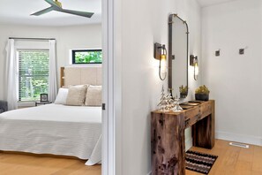 A bedroom with a bed, a wooden console table with a mirror, and a window with blinds.