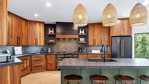 Eine moderne Küche mit Holzschränken, einer zentralen Kochinsel mit Barhocker, einem Edelstahlkühlschrank und einem Gasherd.