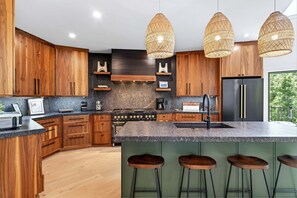 A modern kitchen with wooden cabinets, a central island with bar stools, a stainless steel refrigerator, and a gas stove.