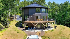 Ein zweistöckiges Haus mit Terrasse, Sitzgelegenheiten im Freien und einem Whirlpool.