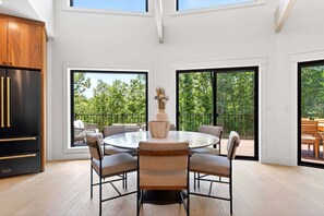 A modern kitchen with a round dining table, chairs, and a large window overlooking a balcony. - Raven House | Pet-Friendly, Hot Tub & Home Gym! (Black Mountain)