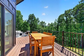 A wooden deck with a table and chairs, a glass door, and a metal railing.