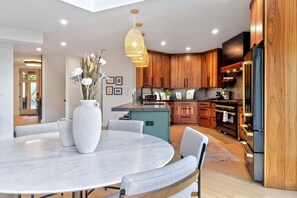 A modern kitchen with wooden cabinets, a marble island, and a large dining table with chairs.