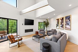 A modern living room with a sofa, armchair, coffee table, and a flat-screen TV. - Raven House | Pet-Friendly, Hot Tub & Home Gym! (Black Mountain)