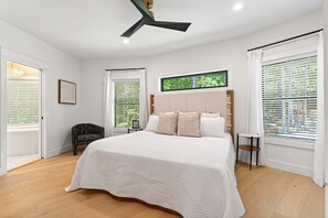 A bedroom with a large bed, a ceiling fan, and a window with blinds.
