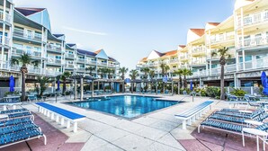 Zona de piscina de un hotel con numerosas tumbonas y bancos, rodeada de edificios de varios pisos con balcones.