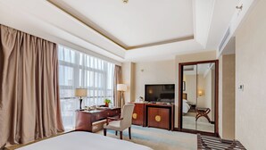 A hotel room with a large bed, a desk with a computer, a TV, and a mirror. - wanxibinguan (Anqing)