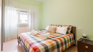 Une chambre à coucher avec une couvre-lit à carreaux, une fenêtre avec des rideaux blancs et une table de chevet avec une lampe.