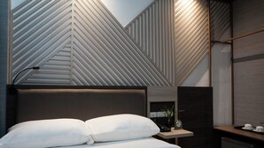 Una habitación de hotel moderna con cama, mesita de noche y pared decorada con patrones geométricos.