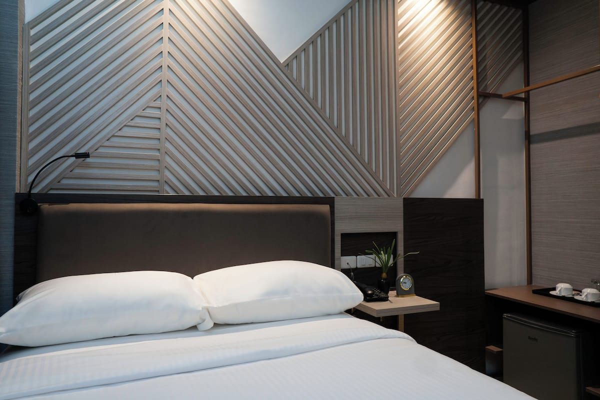 A modern hotel room with a bed, bedside table, and a wall with geometric patterns.