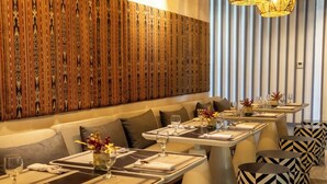 Un restaurante con una larga pared de madera, varias mesas con taburetes de estampado blanco y negro, y un candelabro moderno.