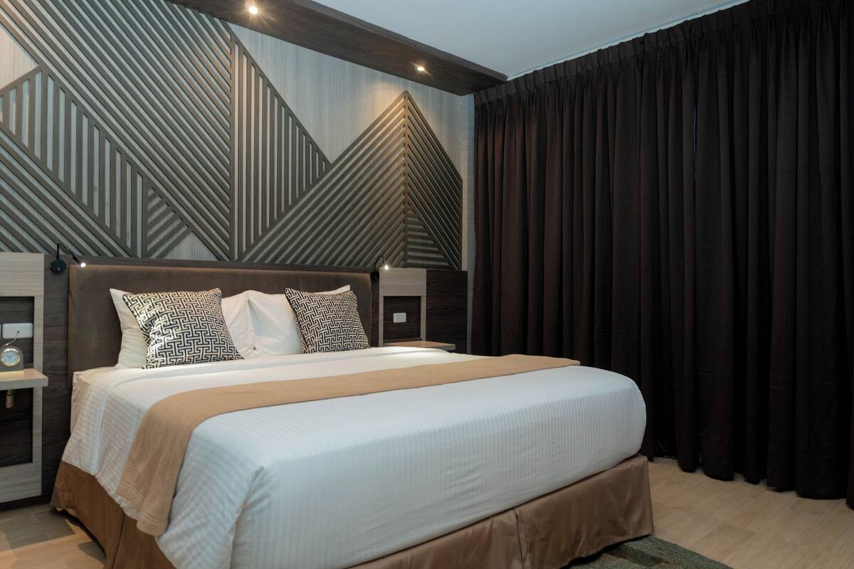A modern hotel room with a large bed, a geometric-patterned wall, and a dark curtain.