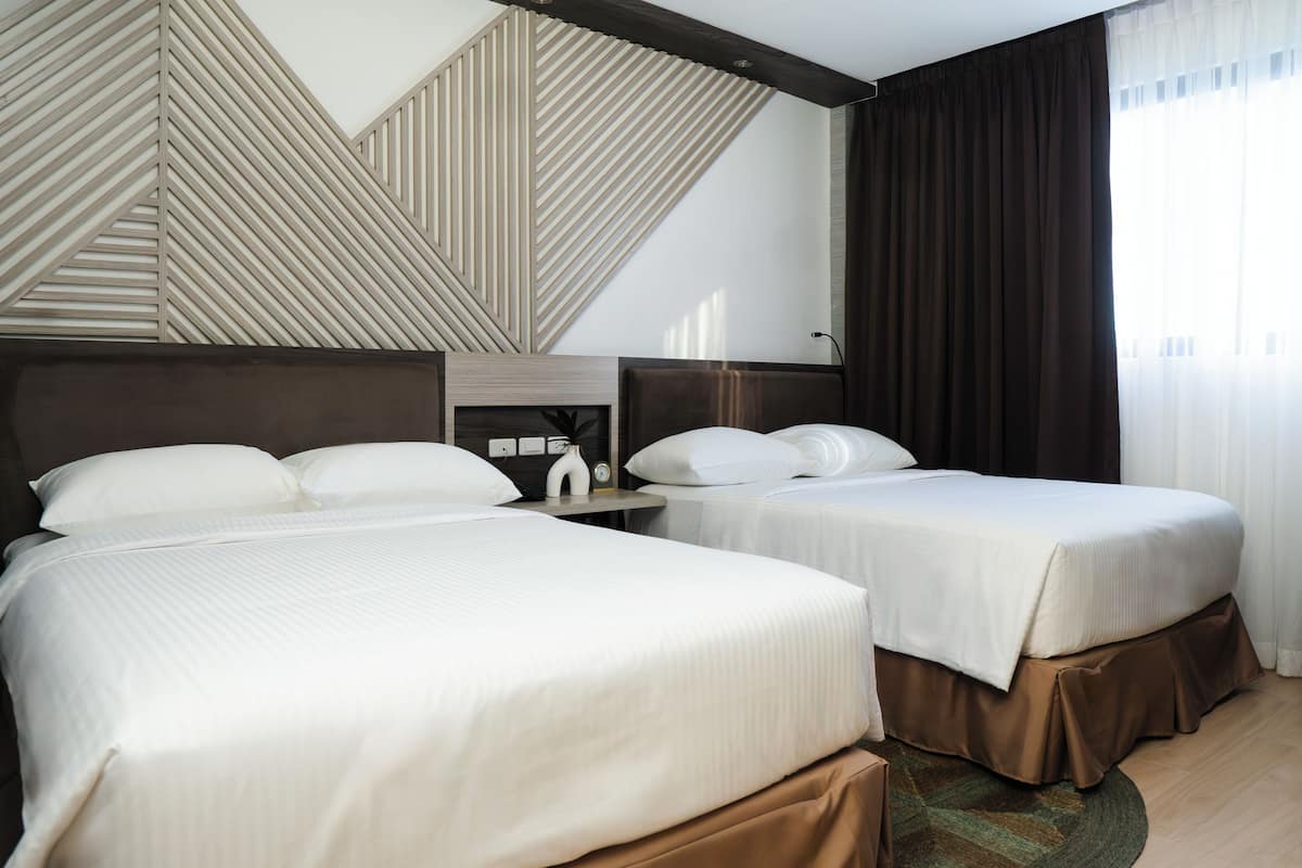 A hotel room with two beds, a wooden headboard, a nightstand, and a large window with curtains.