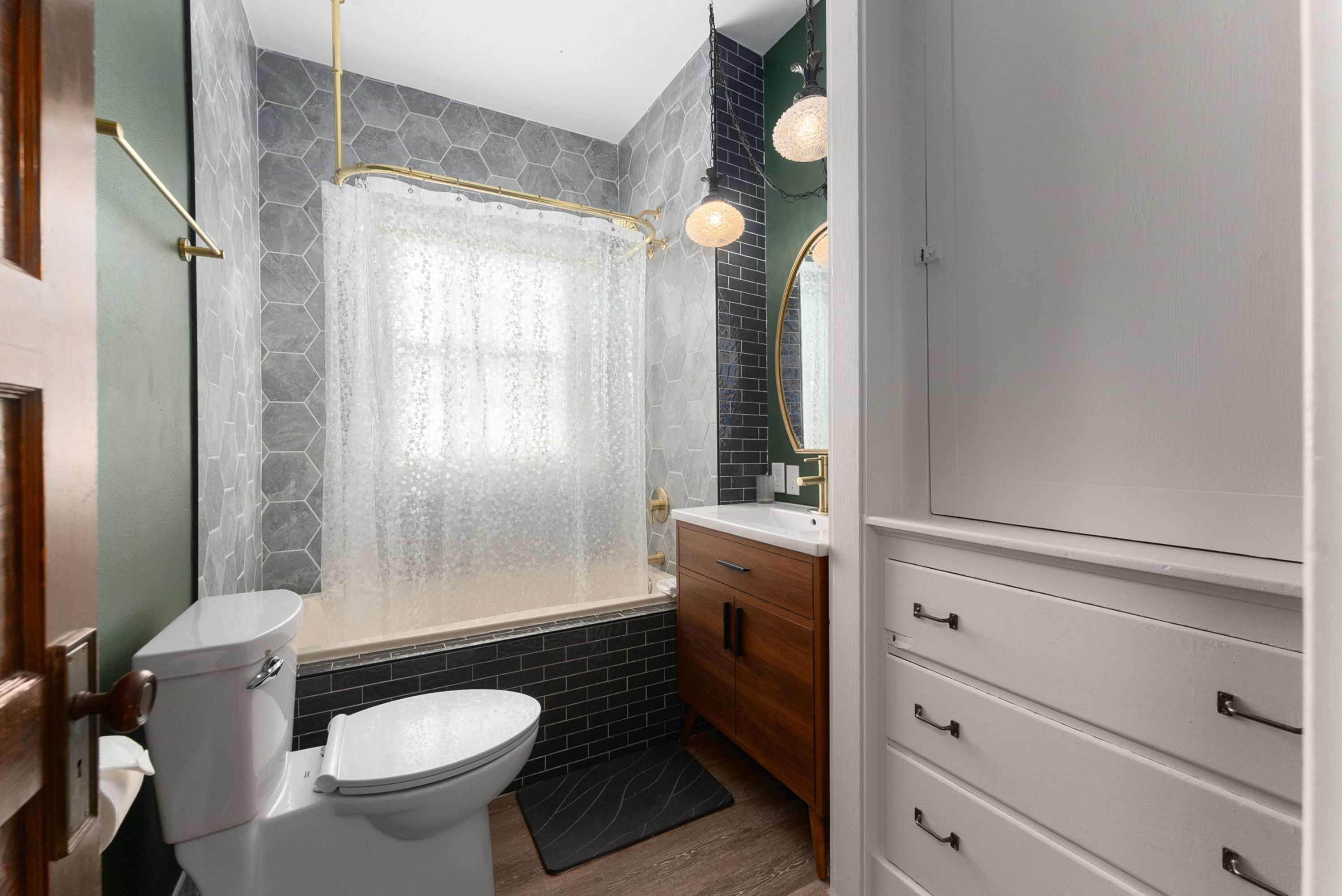A bathroom with a toilet, a bathtub with a shower curtain, a sink, and a vanity with drawers.