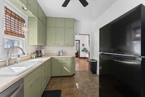 A kitchen with green cabinets, a stainless steel refrigerator, a sink, and a coffee maker.