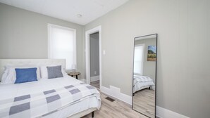 A bedroom with a bed, a mirror, and a door leading to another room.