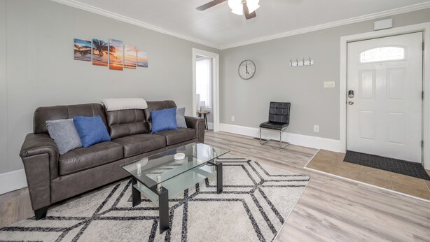 A living room with a brown leather sofa, a glass coffee table, a ceiling fan, and a door with a white frame.