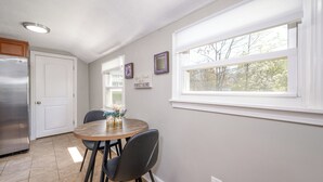 A kitchen with a dining table, chairs, a refrigerator, and a window with a view of trees.