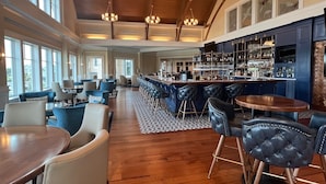 A spacious bar area with high ceilings and large windows, featuring a bar counter, stools, and a seating area with tables and chairs. - Deep Dive by Sandpiper | Near Beach (Seabrook Island)
