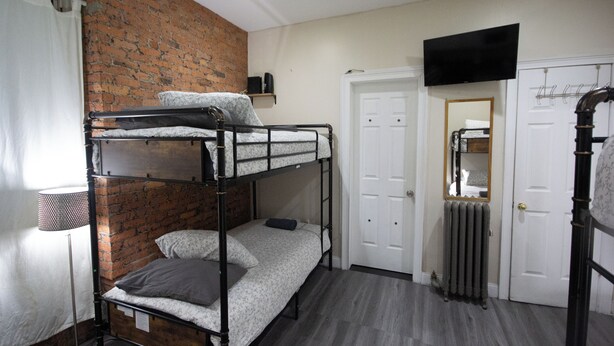 Une chambre avec des lits superposés, un mur en briques, une porte blanche, un radiateur et un téléviseur fixé au mur.