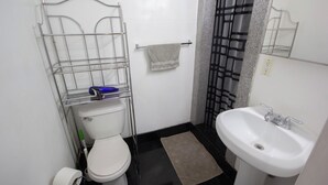 Une petite salle de bain comprenant des toilettes, un lavabo, un porte-serviettes et une étagère en métal.