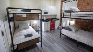 Une chambre de dortoir avec des lits superposés, un coin cuisine et un mur en briques.