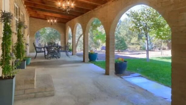 A covered patio area with a wooden ceiling, brick walls, and a view of a green lawn.