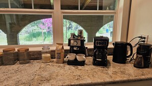 A kitchen counter with a coffee maker, two cups, a jar of sugar, and a bag of coffee.