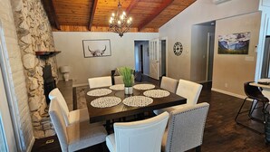 A dining area with a wooden table, white upholstered chairs, and a chandelier.