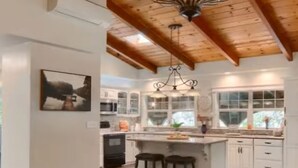 A spacious kitchen with a central island, wooden ceiling beams, and a chandelier.
