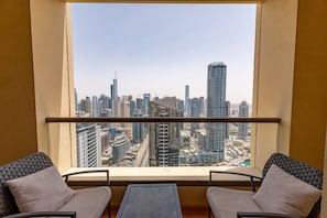 A balcony with two chairs and a table, overlooking a cityscape with high-rise buildings.