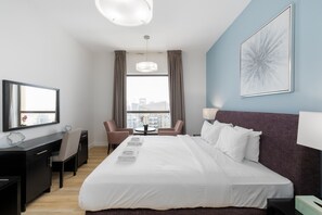 Une chambre d’hôtel avec un grand lit, un bureau, une chaise, une petite table et une fenêtre avec des rideaux.