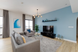 A modern living room with a grey sofa, a glass coffee table, a TV, and a blue accent wall.