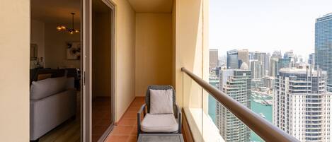 Un balcón con vistas a un paisaje urbano, una puerta corrediza que da a una sala de estar y un sillón acolchado.