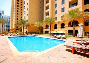 A swimming pool with lounge chairs and palm trees, surrounded by a building with multiple balconies.