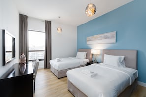 A hotel room with two beds, a desk, and a large window.