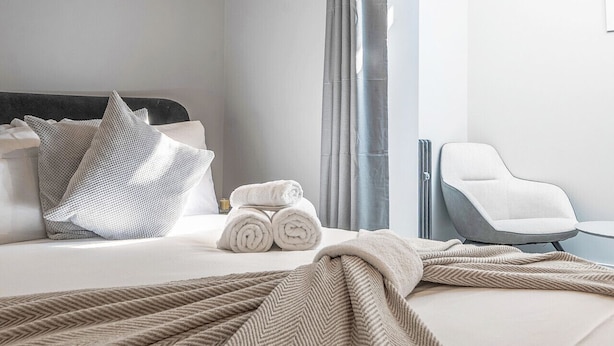 Una habitación de hotel moderna con una cama bien hecha, una silla y un ventanal con cortinas.