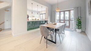 Una cocina moderna con encimera de mármol, comedor con mesa y sillas de madera, y un ventanal con cortinas.