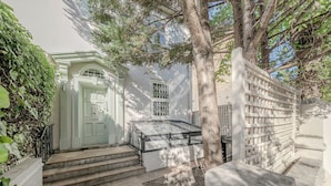 Un edificio blanco con puerta principal, escalones que llevan a ella y un árbol en primer plano.
