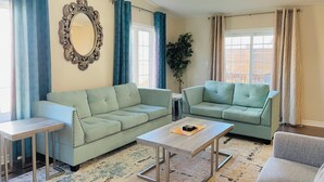 A living room with two light green sofas, a small table, a mirror, and a chandelier.