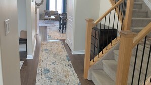 A hallway with a wooden staircase, a rug, and a dining area with a table and chairs.