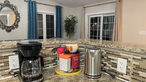 A kitchen with a coffee maker, a toaster, a coffee pot, and a kettle on a granite countertop.
