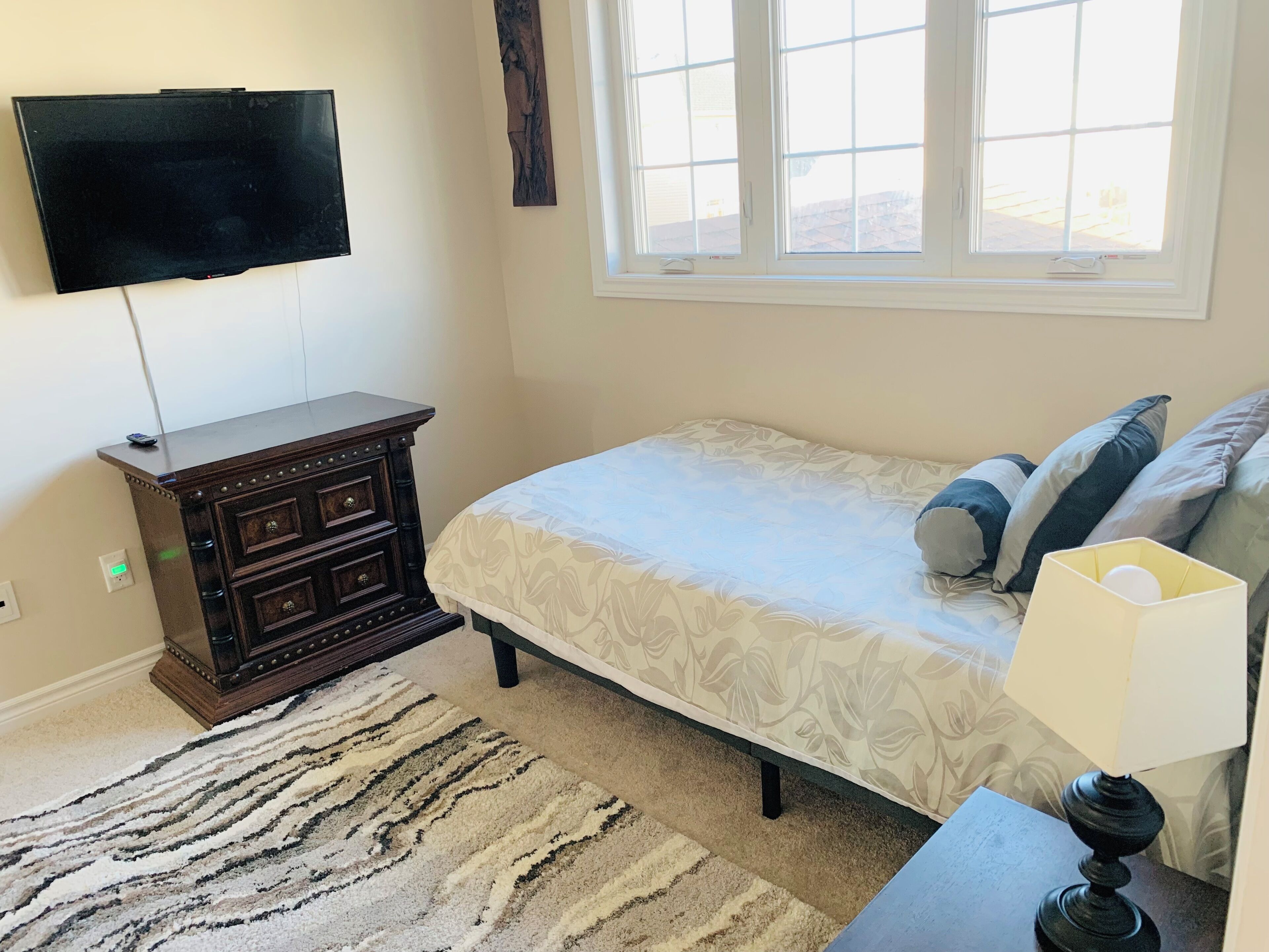 A bedroom with a bed, a dresser, a TV, and a window.