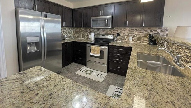 A modern kitchen with dark cabinets, stainless steel appliances, granite countertops, and a backsplash.